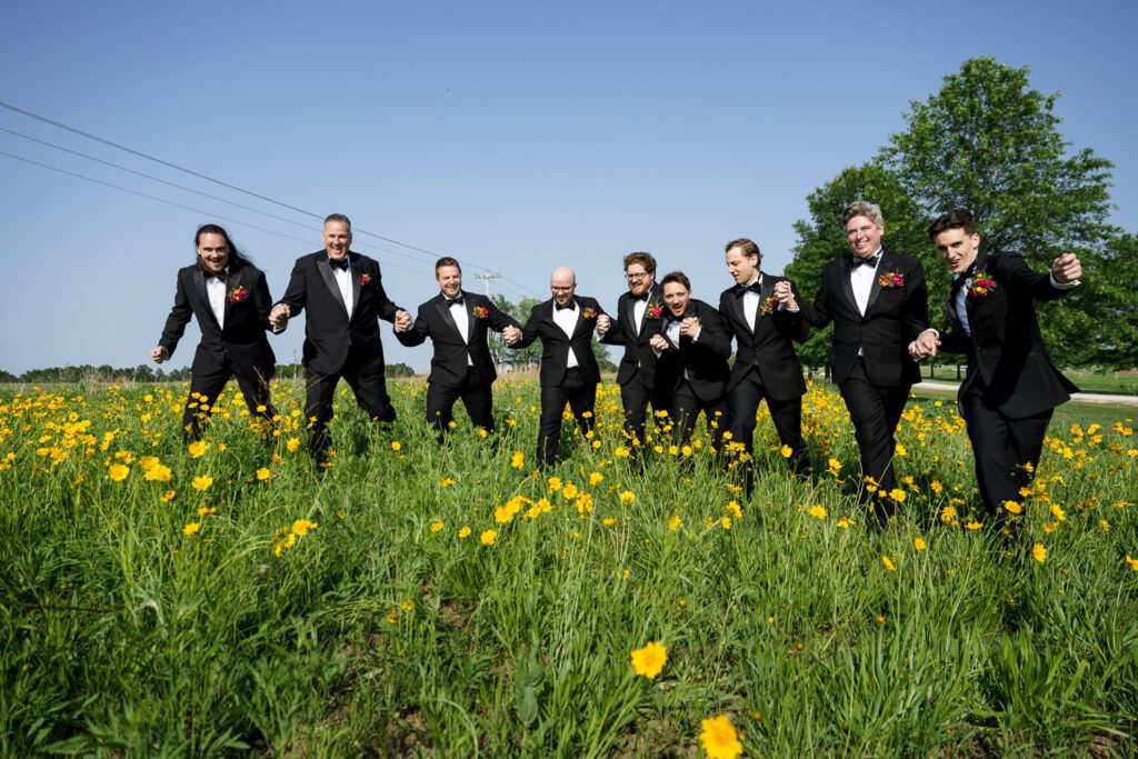 group of groomsmen prance through yellow wild flowers