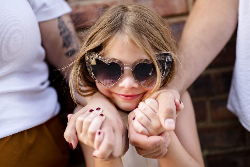 young girl wearing heart glasses and holding parents hands close
