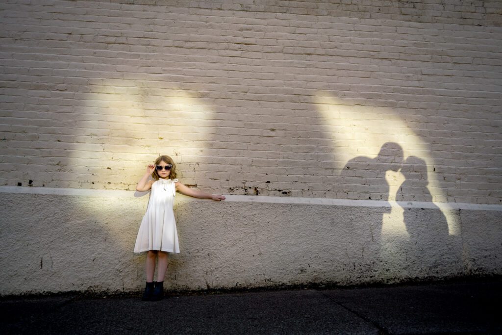 young girl stands in spot light of sun while her parents shadows show them kissing