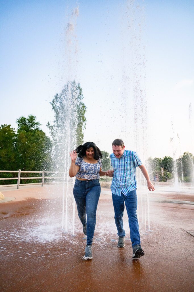 young couple run through water fountains