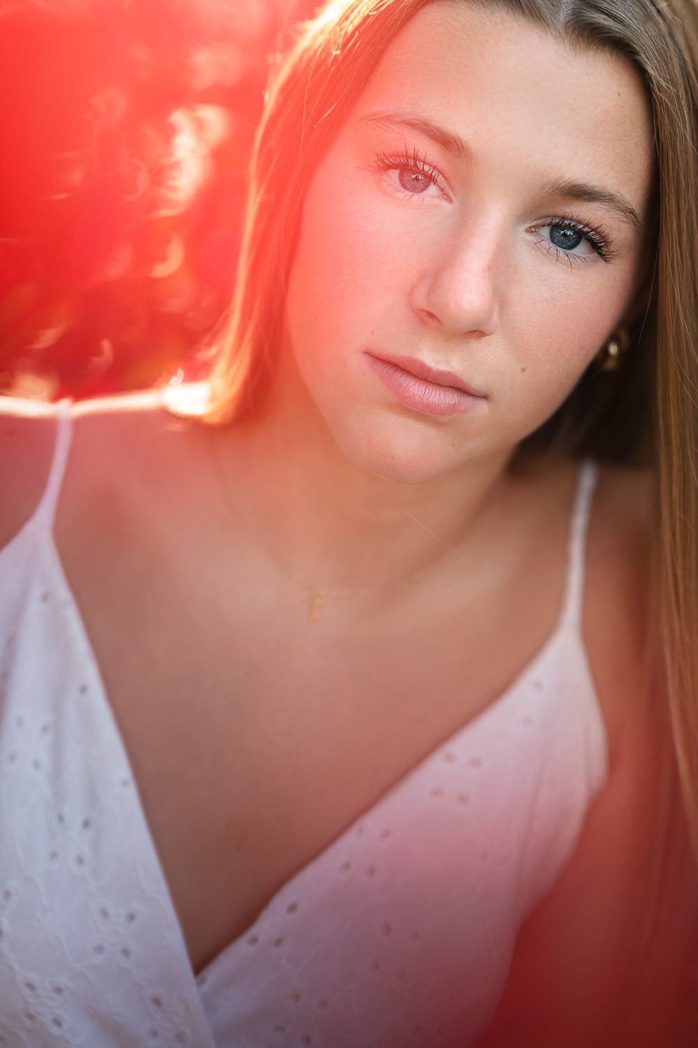 senior girl stares into camera with red flowers blurred in shot