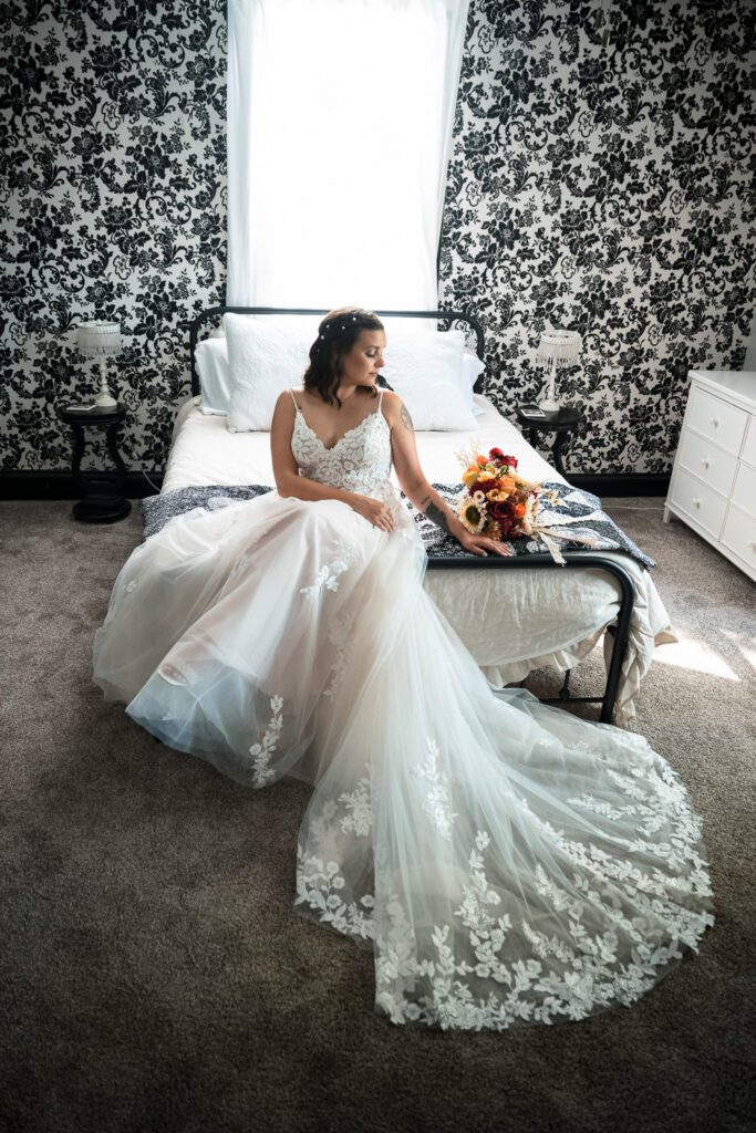 bride sits on bed in front of black and white wall paper