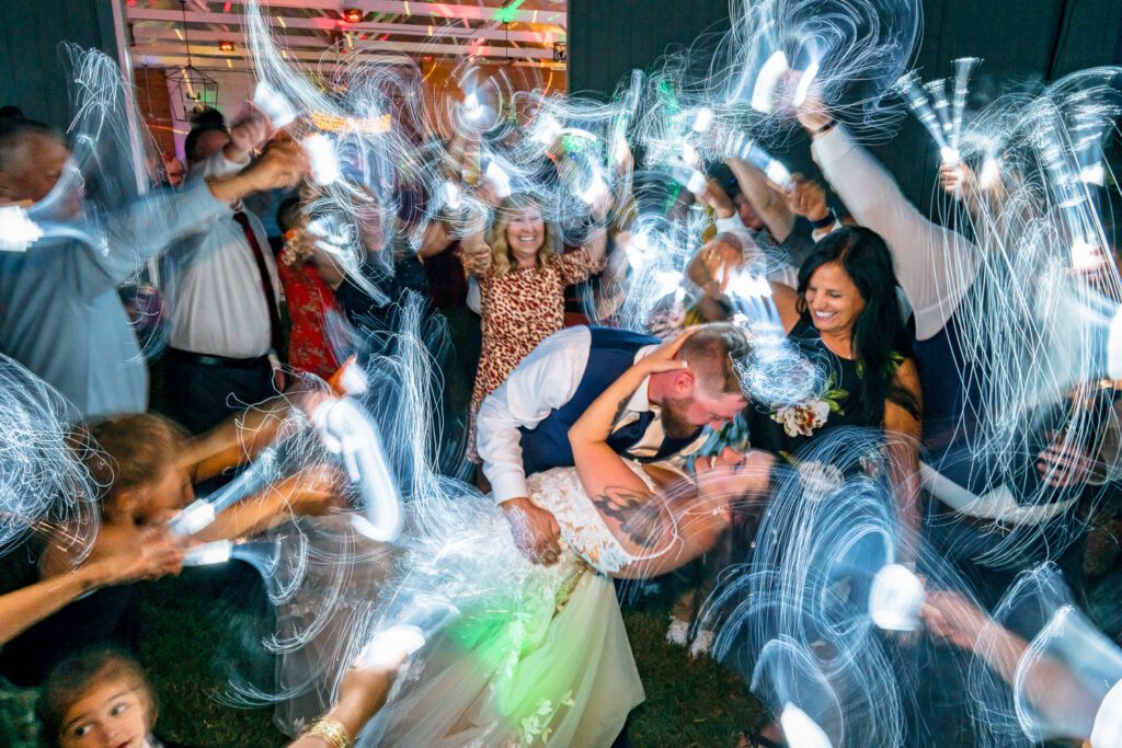 bride and groom kiss with crowd surrounding them waiving light wands