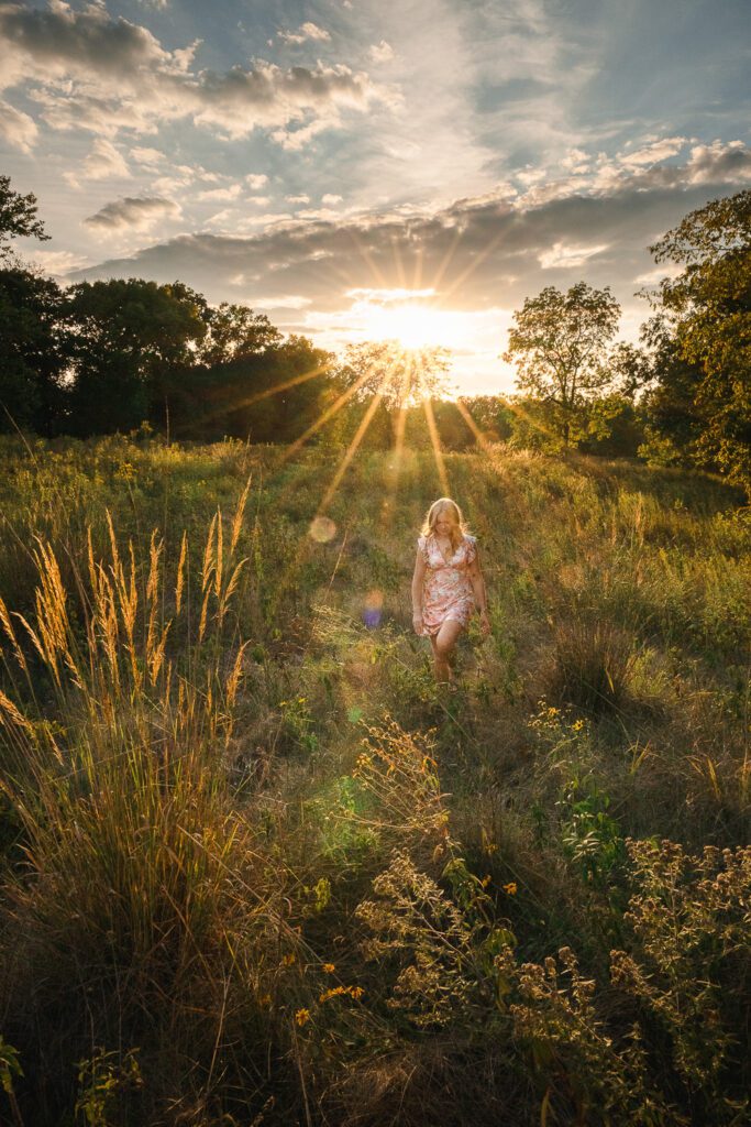 senior girl wearing dress walks in field with sun flair