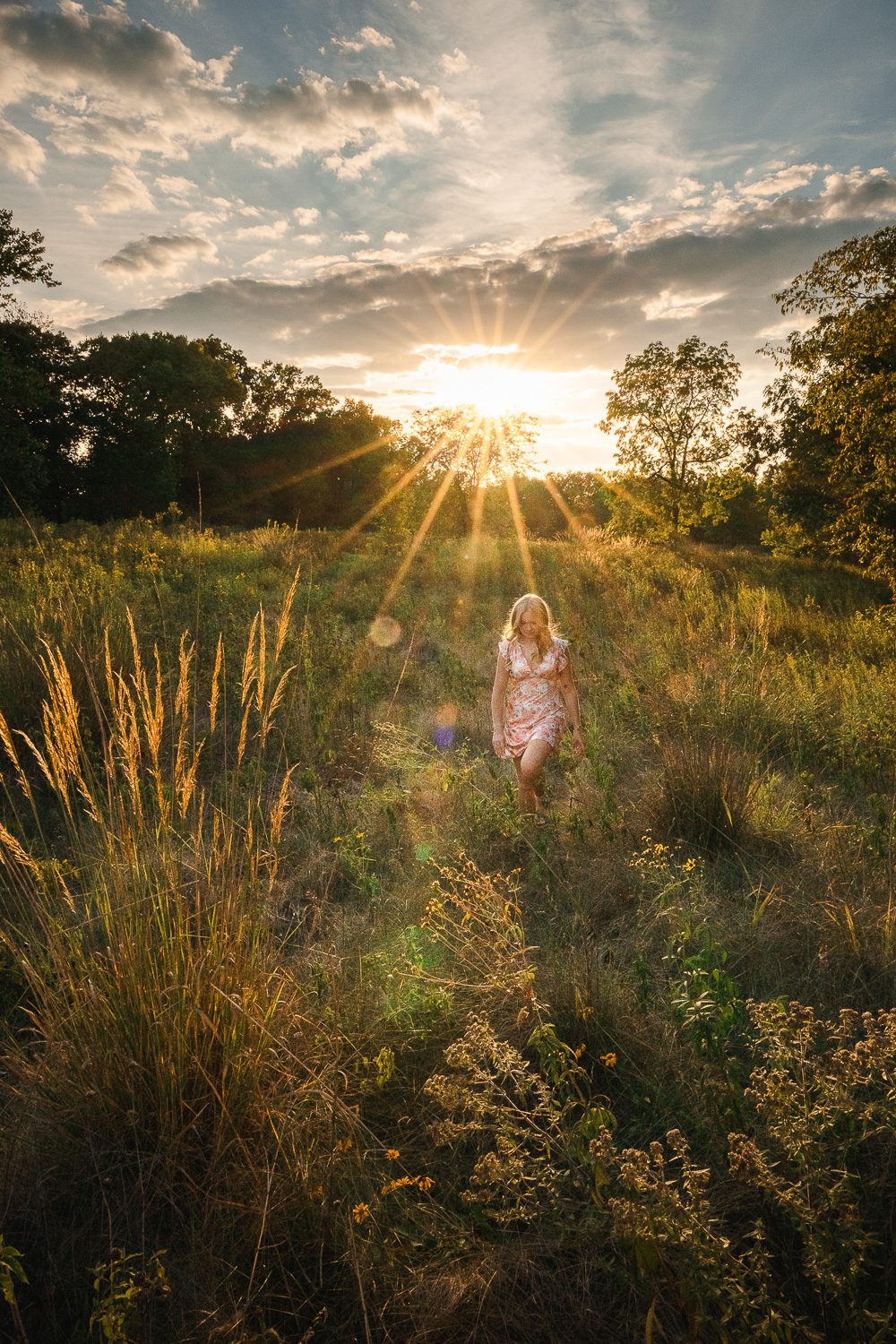 senior girl wearing dress walks in field with sun flair 