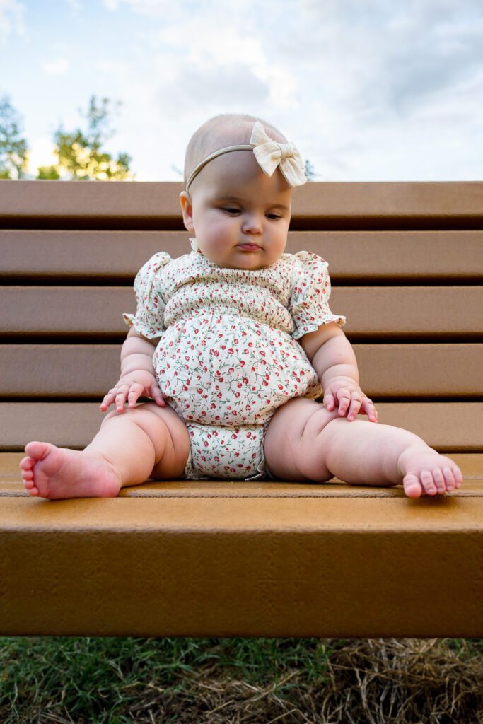 Baby girl with cute chubby legs sits on park bench