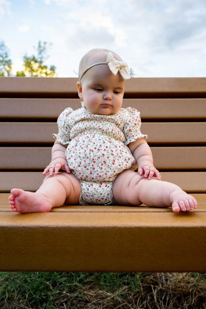 Baby girl with cute chubby legs sits on park bench