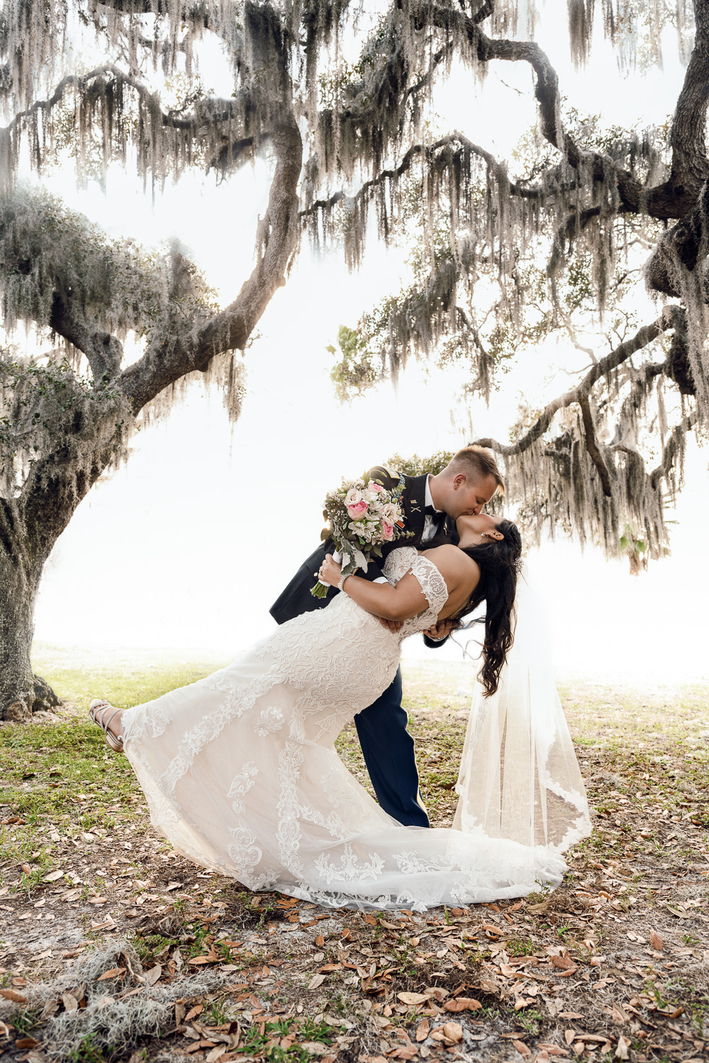 Army soldier kisses bride as he dips her in front of spanish moss covered trees