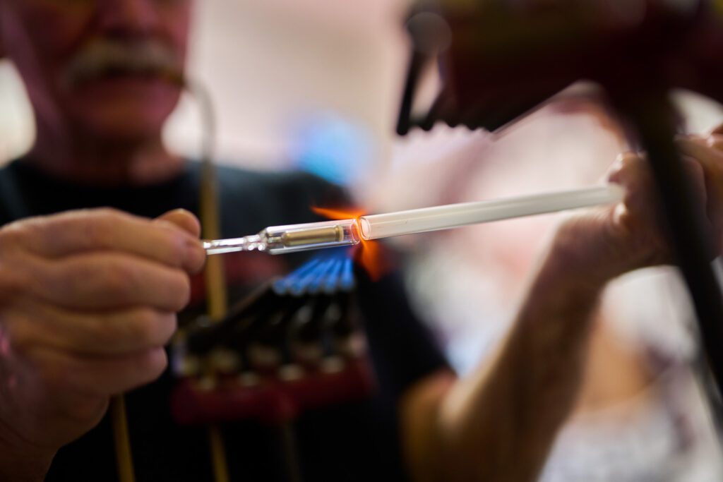 Jim McCarter of Creative Neon in Columbia, Mo blows air through a silicone tube as he heats glass neon tubes in a cross burner.