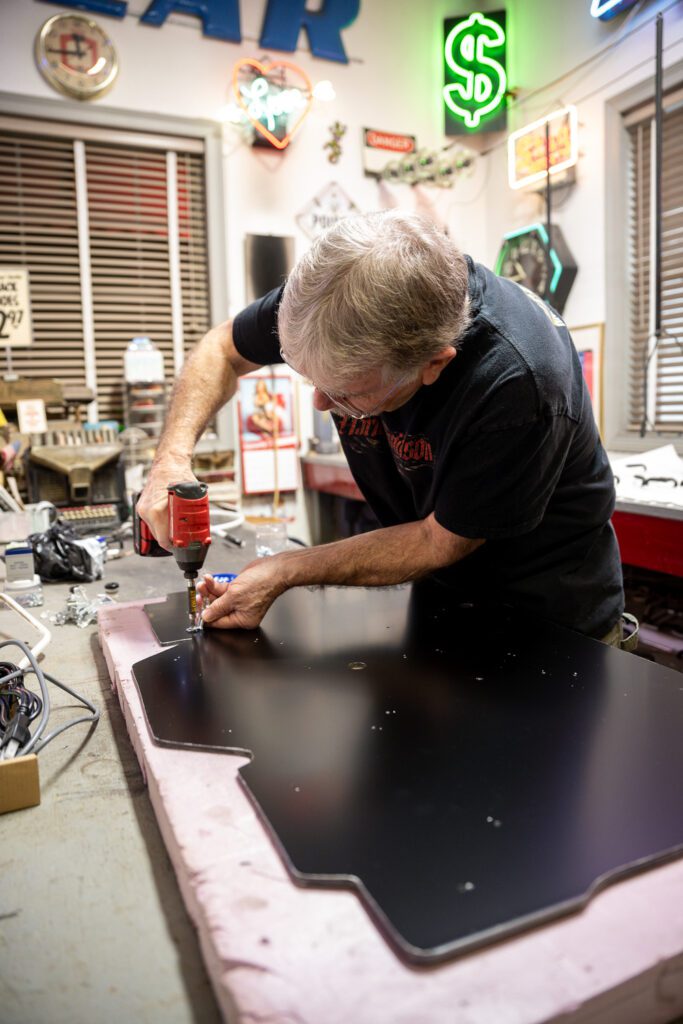 Neon glass bender attaching clear spacers to neon sign