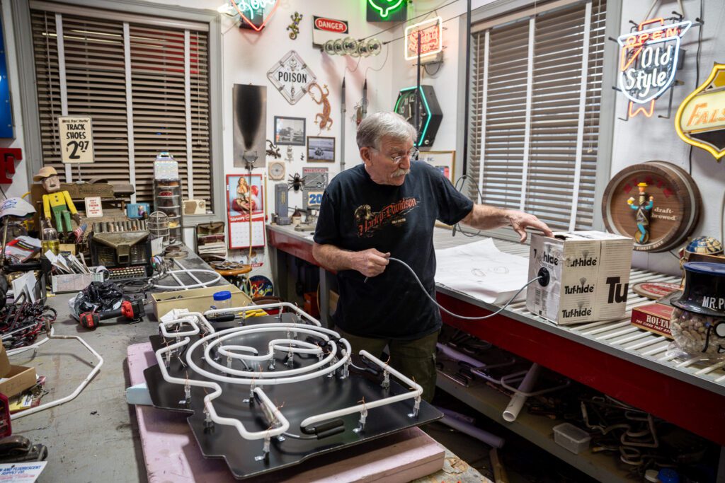 Neon Sign glass bender Jim McCarter pulls wire from a box to connect neon tubing.