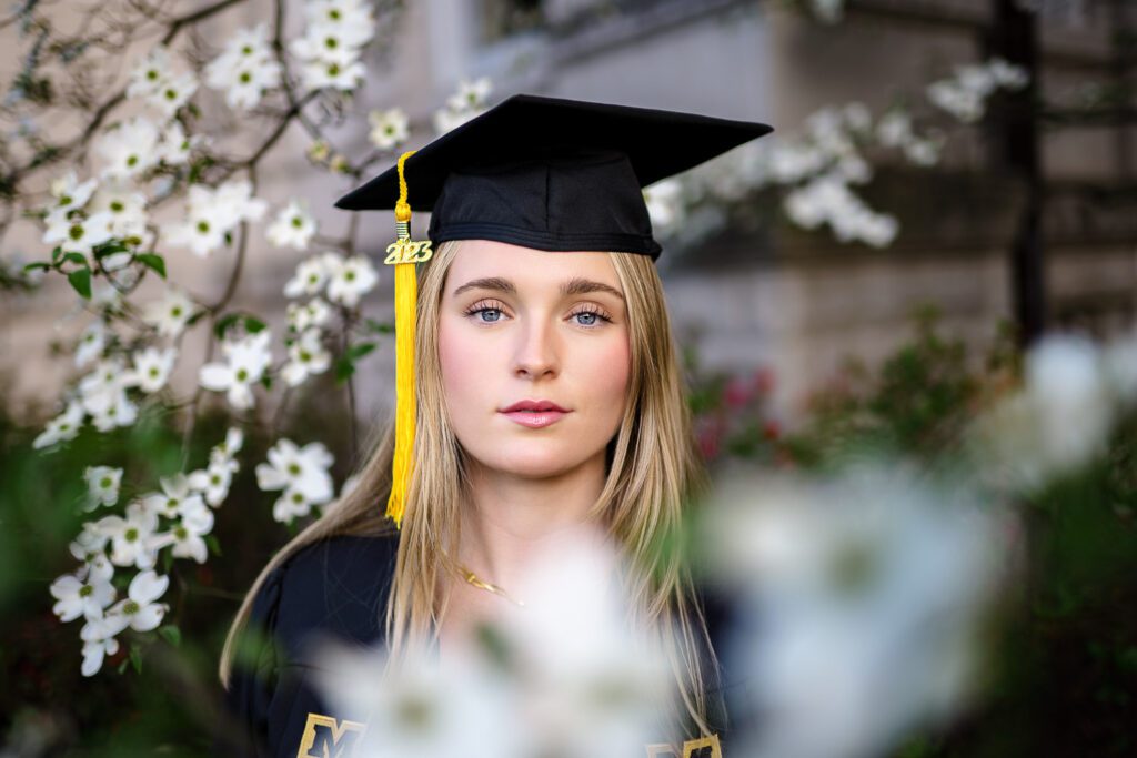 Blonde senior girl wearing mortar board looks through white blooming tree