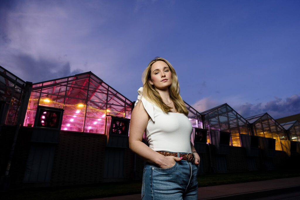 senior woman wearing blue jeans standing in front of colorful greenhouses