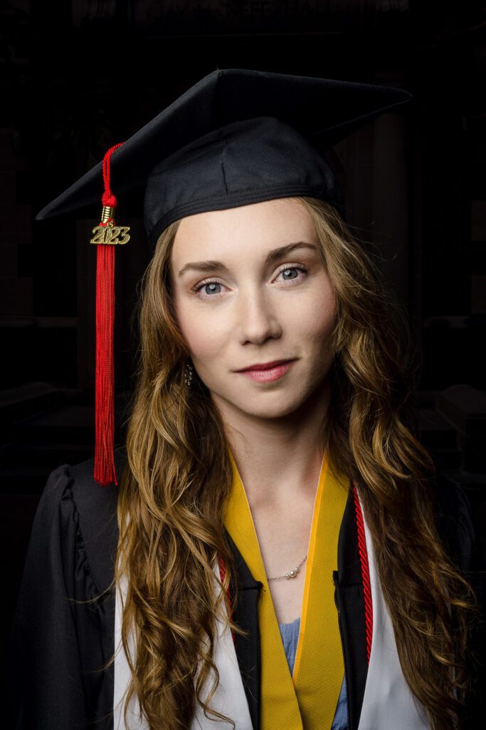 senior portrait brunette woman wearing cap and gown black background