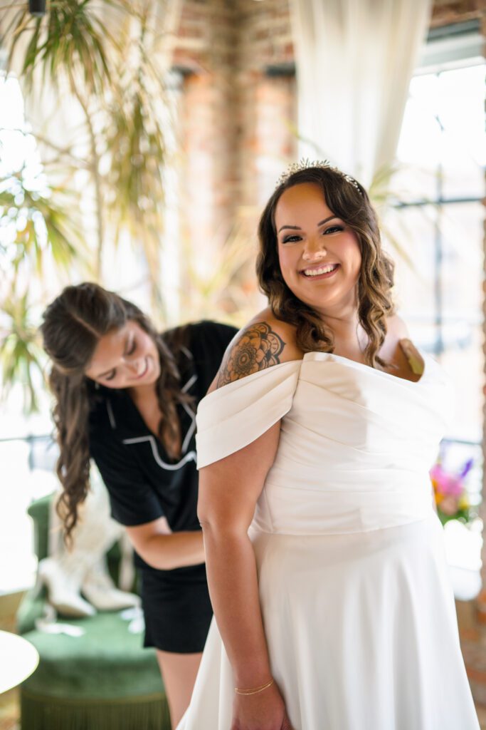 bride getting her dress zipped up while smiling