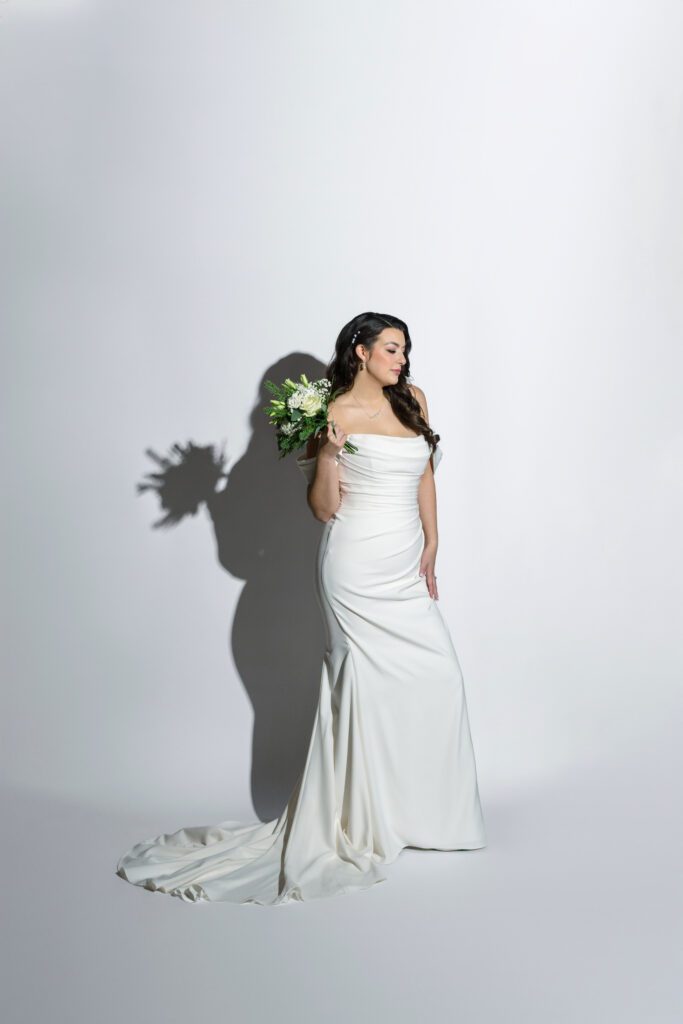 bride poses with flowers on white backdrop on wedding day with hard light