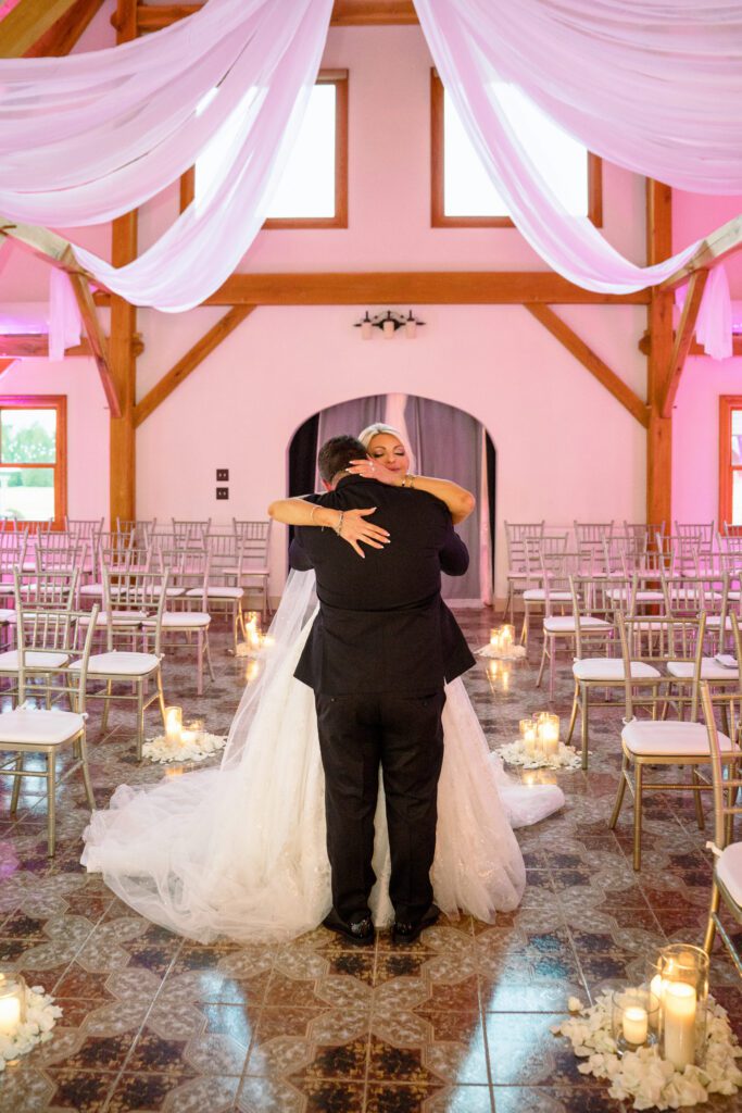 bride and groom hug in wedding venue with pink light