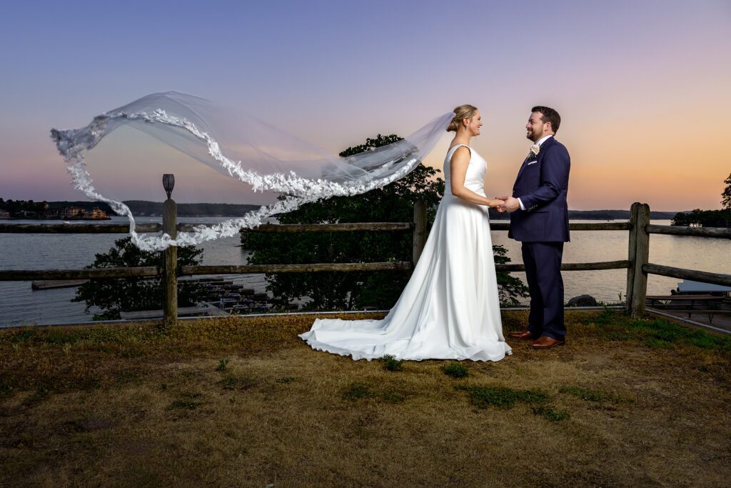 bride and groom standing by lake ozark veil blowing in wind