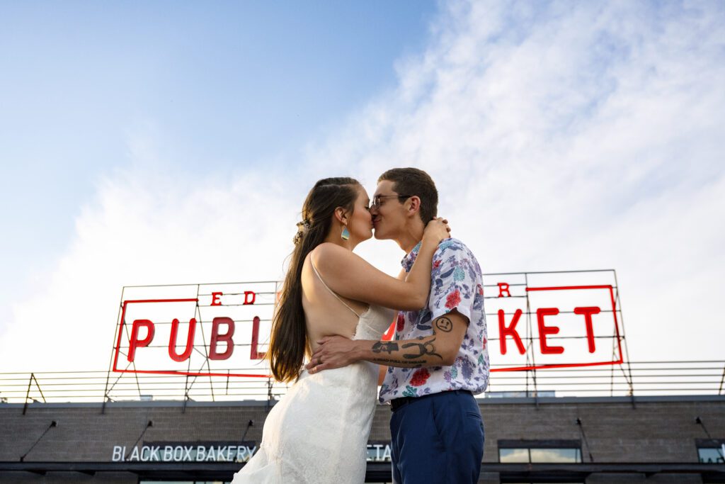 bride and groom kiss in front of colorado public market sign