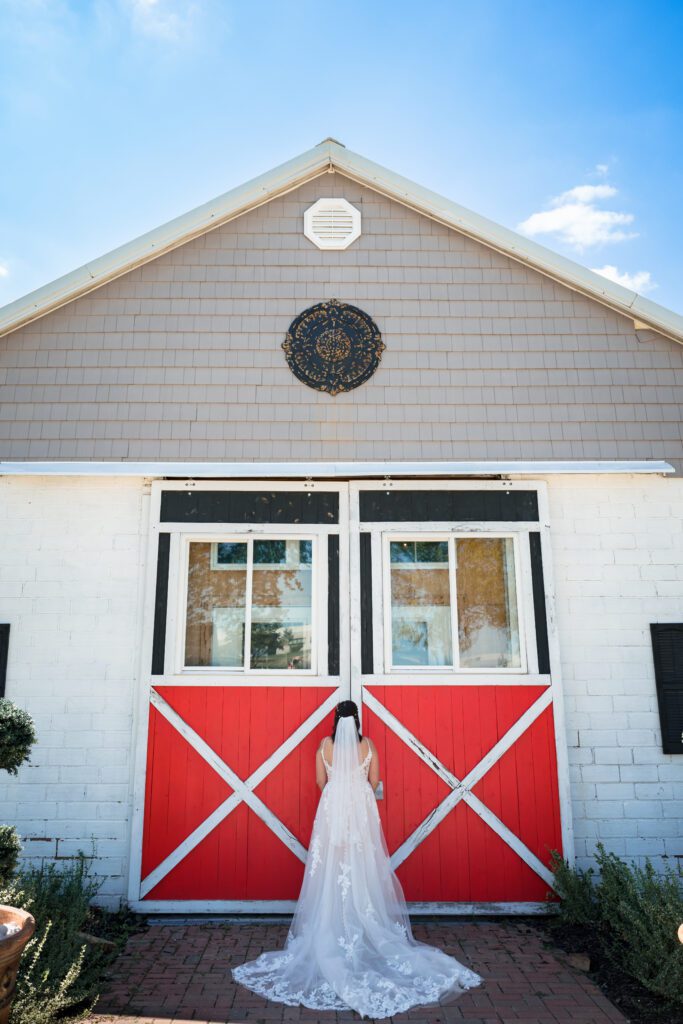 bride stands in front of red barn door
