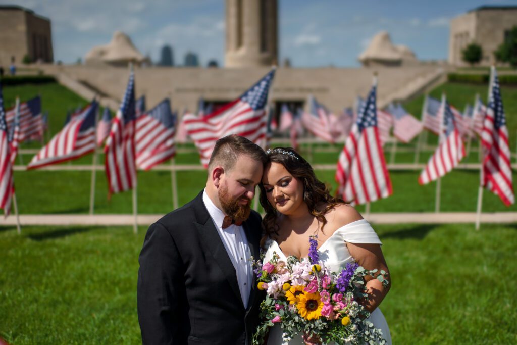 bride and groom touch heads in front of flags at World War One Memorial in Kansas City Missouri